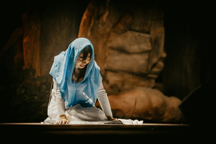 A woman in a blue headscarf kneels on the ground